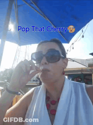 A Woman Wearing Sunglasses Is Sitting Under An Umbrella With The Words Pop That Cherry Written Above Her GIF