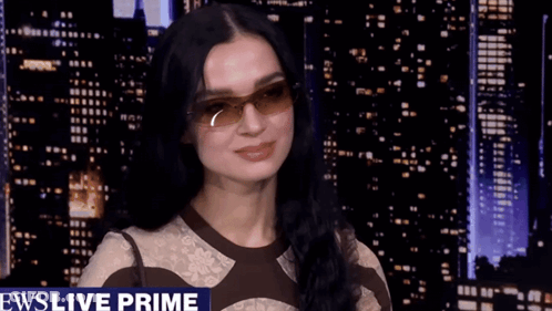 A Woman Wearing Sunglasses Is Smiling In Front Of A News Live Prime Banner GIF