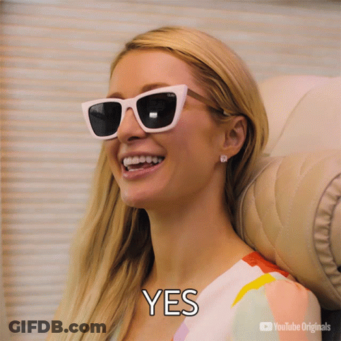 A Woman Wearing Sunglasses Is Smiling With The Word Yes Below Her GIF