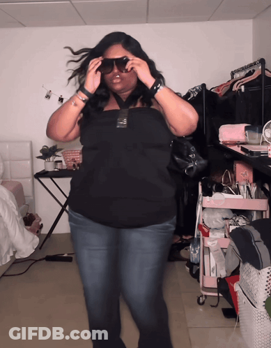 A Woman Wearing Sunglasses Is Standing In A Room With A Pink Cart GIF
