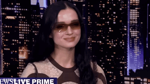 A Woman Wearing Sunglasses Is Standing In Front Of A News Live Prime Banner GIF