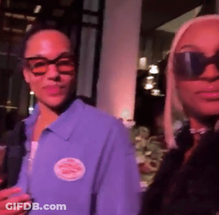 A Woman Wearing Sunglasses Is Standing Next To A Man Wearing A Purple Shirt . GIF