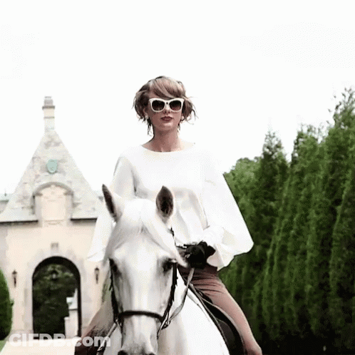 A Woman Wearing Sunglasses Rides A White Horse In Front Of A Building GIF