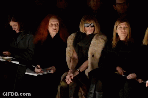 A Woman Wearing Sunglasses Sits In A Dark Room GIF