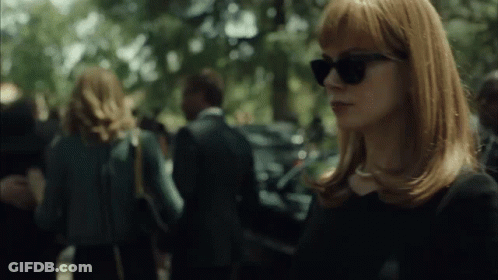 A Woman Wearing Sunglasses Stands In A Crowded Area GIF
