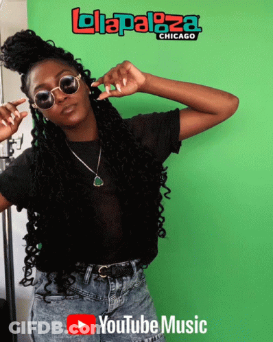 A Woman Wearing Sunglasses Stands In Front Of A Green Screen That Says ' Lolapaloza Chicago ' On It GIF