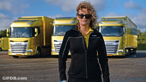 A Woman Wearing Sunglasses Stands In Front Of Yellow Daf Trucks GIF