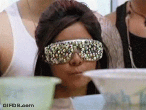 A Woman Wearing Sunglasses With Rhinestones On Them Is Sitting At A Table GIF