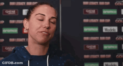 A Woman Wipes Her Face With A Towel In Front Of A Wall That Says Qatar On It GIF