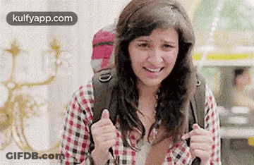 A Woman With A Backpack Is Smiling And Giving A Thumbs Up Sign . GIF