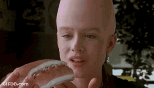 A Woman With A Bald Head Is Holding A Hot Dog . GIF