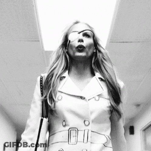A Woman With A Bandage On Her Eye Is Walking Down A Hallway With A Purse . GIF
