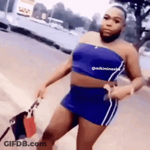 A Woman With A Beard Is Wearing A Blue Top And Shorts And Holding A Bag . GIF