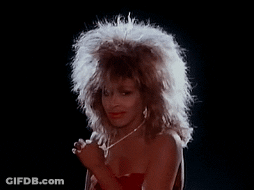 A Woman With A Big Afro Is Singing Into A Microphone While Wearing A Red Dress And A Necklace . GIF
