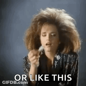 A Woman With A Big Hairdo Is Holding A Feather In Her Hand And Saying Or Like This . GIF