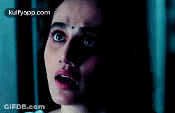 A Woman With A Bindi On Her Forehead Is Looking At The Camera In The Dark . GIF