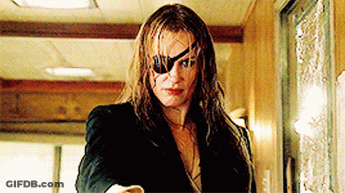 A Woman With A Blindfold On Her Eye Is Standing In A Hallway . GIF