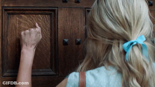 A Woman With A Blue Bow In Her Hair Knocks On A Door GIF