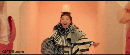 A Woman With A Box On Her Head Is Wearing A Striped Outfit GIF