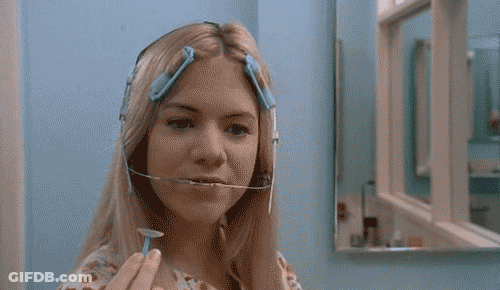 A Woman With A Brace On Her Head Holds A Razor In Front Of A Mirror GIF