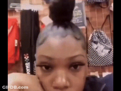 A Woman With A Bun On Her Head Is Sitting In Front Of A Wall With Clothes Hanging On It . GIF