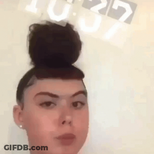 A Woman With A Bun On Her Head Is Standing In Front Of A Clock That Reads 10:29 GIF