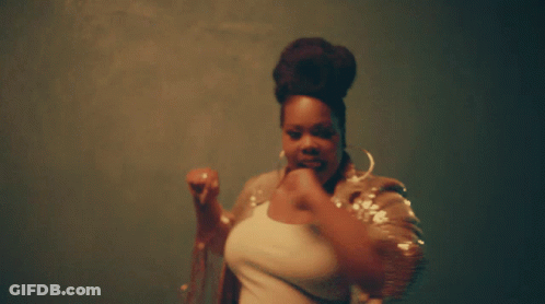 A Woman With A Bun On Her Head Is Wearing Hoop Earrings And A Sequined Jacket GIF