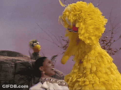A Woman With A Crown On Her Head Stands Next To A Big Bird GIF