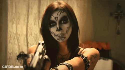 A Woman With A Day Of The Dead Makeup On Her Face Holds A Gun GIF