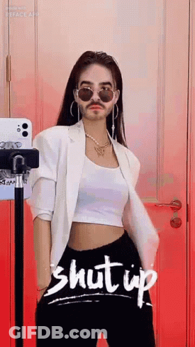 A Woman With A Fake Mustache And Sunglasses Is Standing In Front Of A Red Wall . GIF