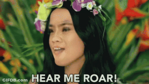 A Woman With A Flower Crown On Her Head Is Standing In Front Of A Flower Garden . GIF