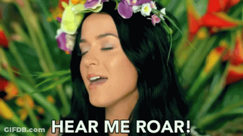 A Woman With A Flower Crown On Her Head Is Standing In Front Of Flowers And Says `` Hear Me Roar '' . GIF
