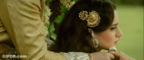 A Woman With A Flower In Her Hair Is Being Held By A Man In A Gold Suit GIF
