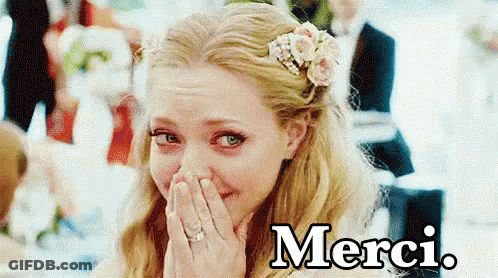 A Woman With A Flower In Her Hair Is Covering Her Face With Her Hands And The Word Merci Is On The Bottom GIF