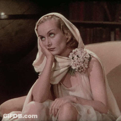 A Woman With A Flower In Her Hair Is Sitting In A Chair With Her Hand On Her Face GIF