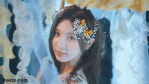 Woman With Flower In Hair Standing In Front Of Curtain GIF