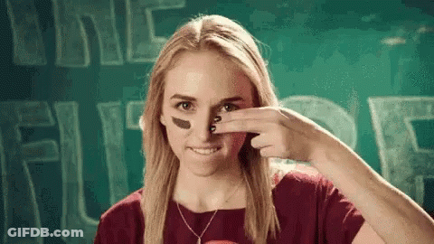 A Woman With A Football On Her Face Is Smiling And Covering Her Nose With Her Hand . GIF