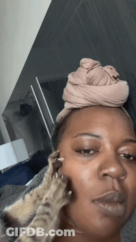 A Woman With A Head Scarf On Her Head Is Being Petted By A Cat GIF