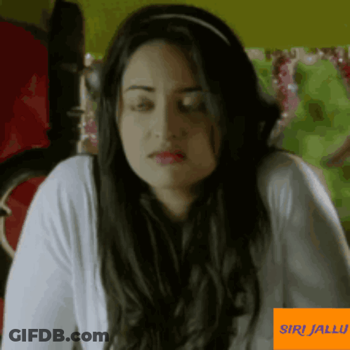 A Woman With A Headband On Her Head Is Sitting In Front Of A Sign That Says Siri Jallu GIF