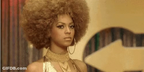 A Woman With A Large Afro Is Wearing A Gold Dress And Hoop Earrings . GIF