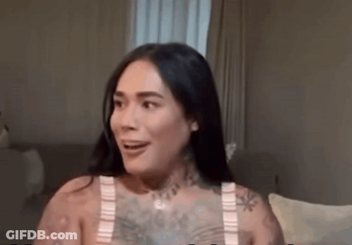 A Woman With A Lot Of Tattoos Is Sitting On A Couch And Smiling . GIF