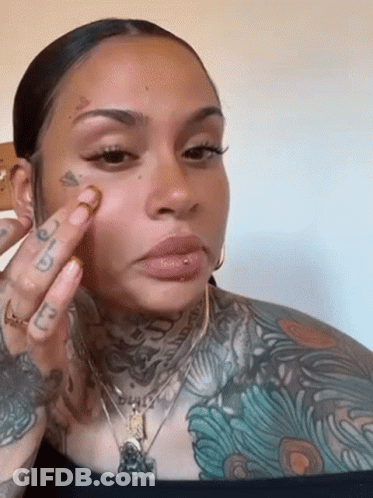 A Woman With A Lot Of Tattoos On Her Face Is Applying Makeup . GIF