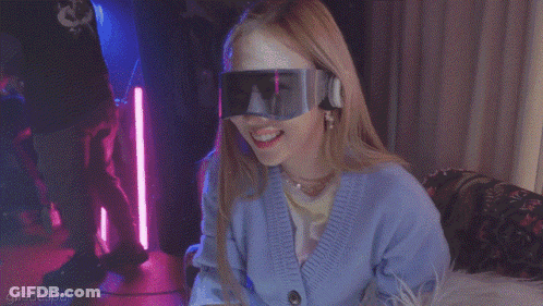 A Woman With A Mask On Her Face Is Wearing A Blue Cardigan And Goggles GIF