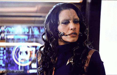 A Woman With A Microphone On Her Face Is Standing In Front Of A Computer Screen GIF