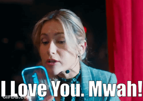 A Woman With A Microphone On Her Neck Is Holding A Cell Phone And Says I Love You Mwah GIF