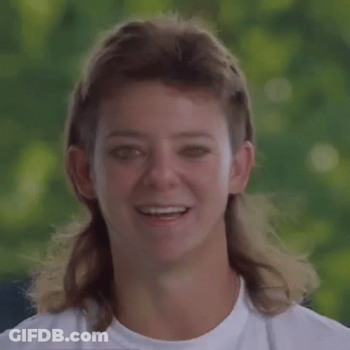 A Woman With A Mullet And A White Shirt Smiles GIF