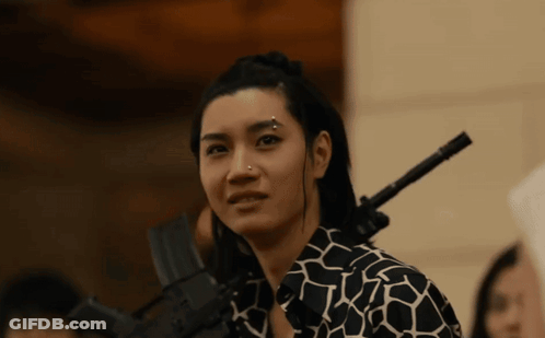A Woman With A Piercing On Her Nose Is Holding A Gun On Her Shoulder GIF