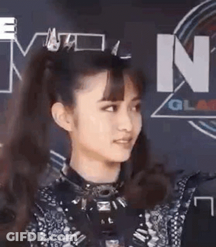 A Woman With A Ponytail Is Standing In Front Of A Sign That Says ' N ' On It . GIF