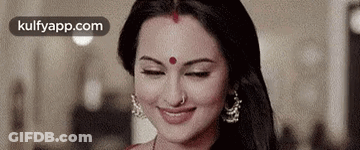 A Woman With A Red Bindi On Her Forehead Is Smiling And Looking Down . GIF
