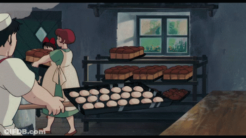 A Woman With A Red Bow On Her Head Is Standing Next To A Man In A Bakery Holding A Loaf Of Bread GIF